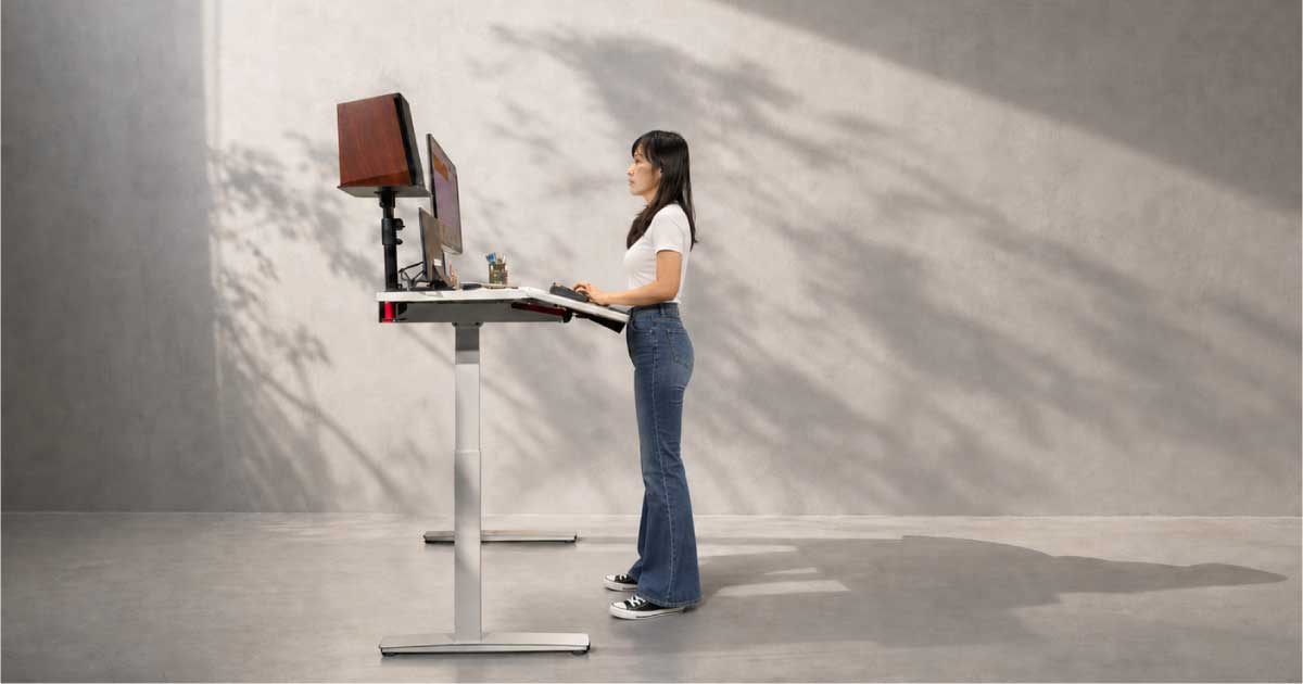 User adjusting a Niture TILT standing desk with relaxed shoulders and keyboard near elbow height